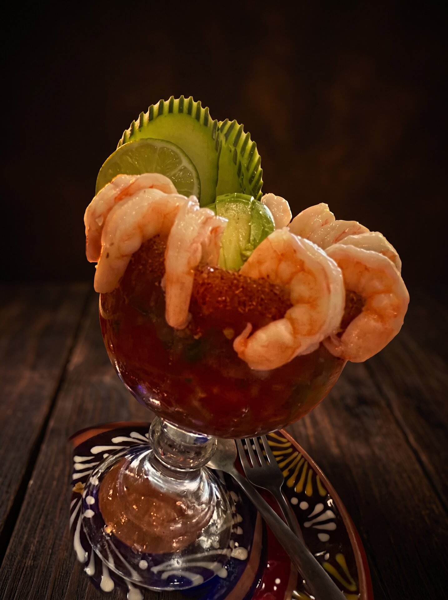 Coctel de camarón in a footed glass, shrimp hooked over the rim with cucumber and lime