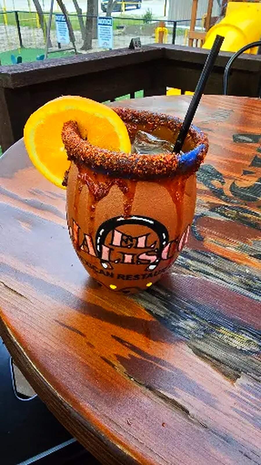 A michelada in a branded clay mug on the patio table, orange slice on the rim