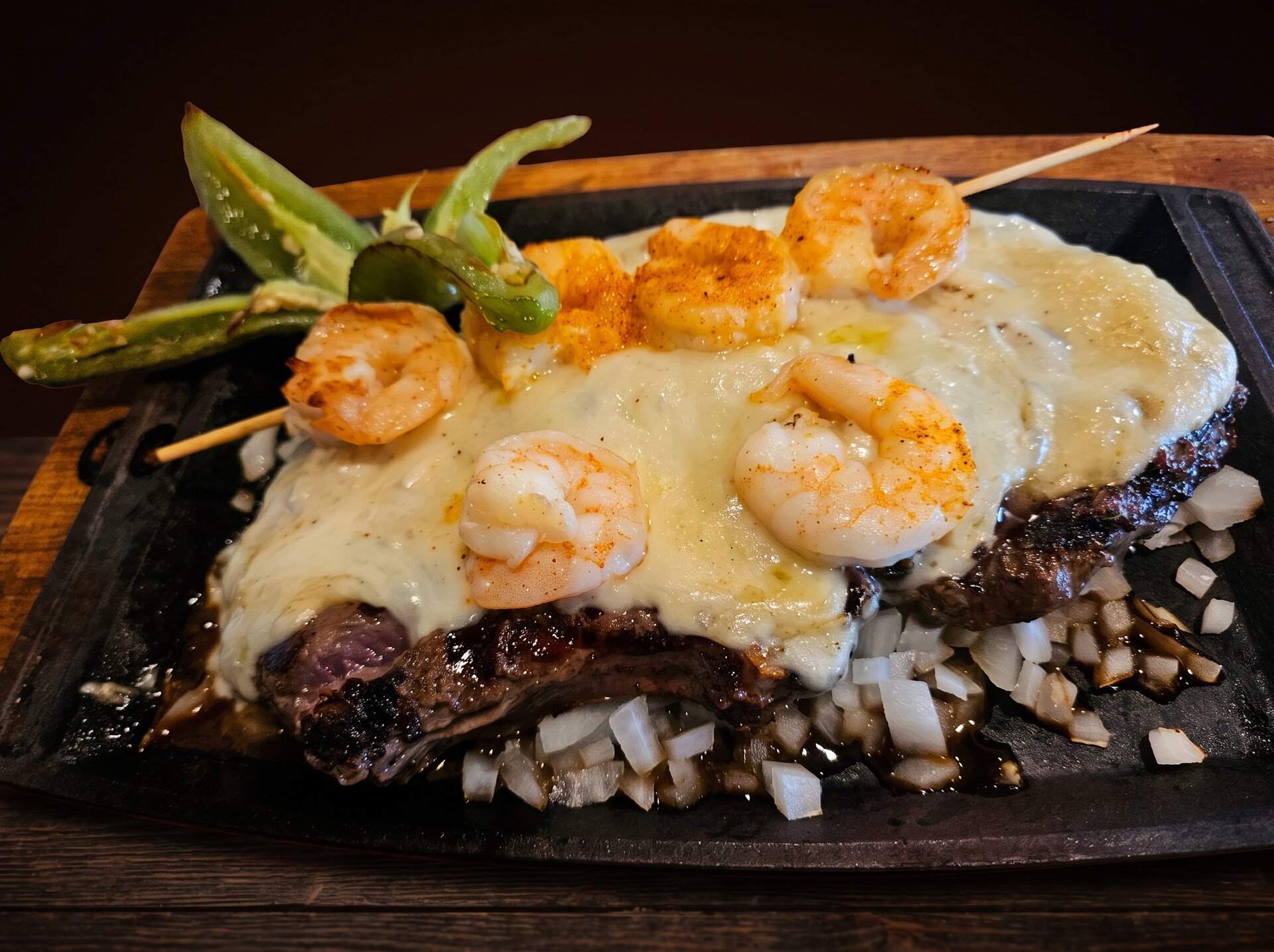 Steak flameado on a sizzling plate under melted cheese, topped with shrimp and grilled chiles